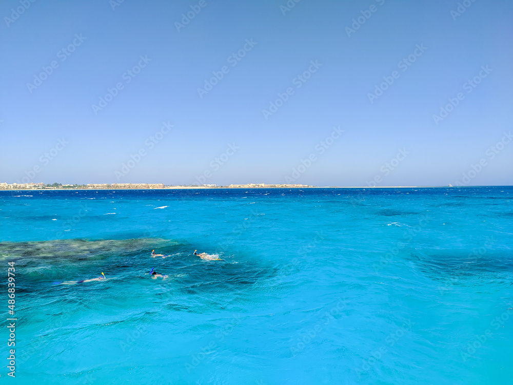 People swim and snorkel near a coral reef in the azure red sea. Copy space. Hurghada, Egypt.