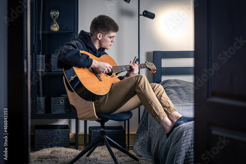 Konstfotografi A young man plays the acoustic guitar in his room at home.