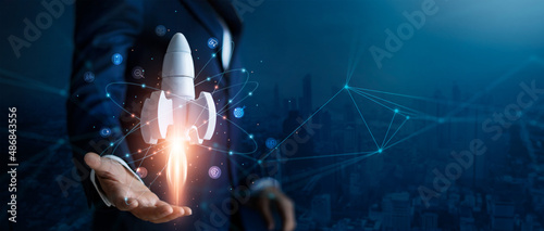 Startup business concept, Businessman control white rocket is launching and soar flying out from hand to sky for growth business,  Fast business success. Network connection on city background. photo