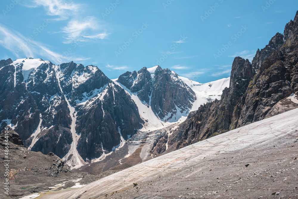 Scenic mountain landscape with glacier under sharp rocks in sunlight. Awesome landscape with glacial tongue and rocky pinnacle in sunshine. Beautiful view to snow mountains at very high altitude. Scenic mountain landscape with glacier under sharp rocks in sunlight. Awesome landscape with glacial tongue and rocky pinnacle in sunshine. Beautiful view to snow mountains at very high altitude.
