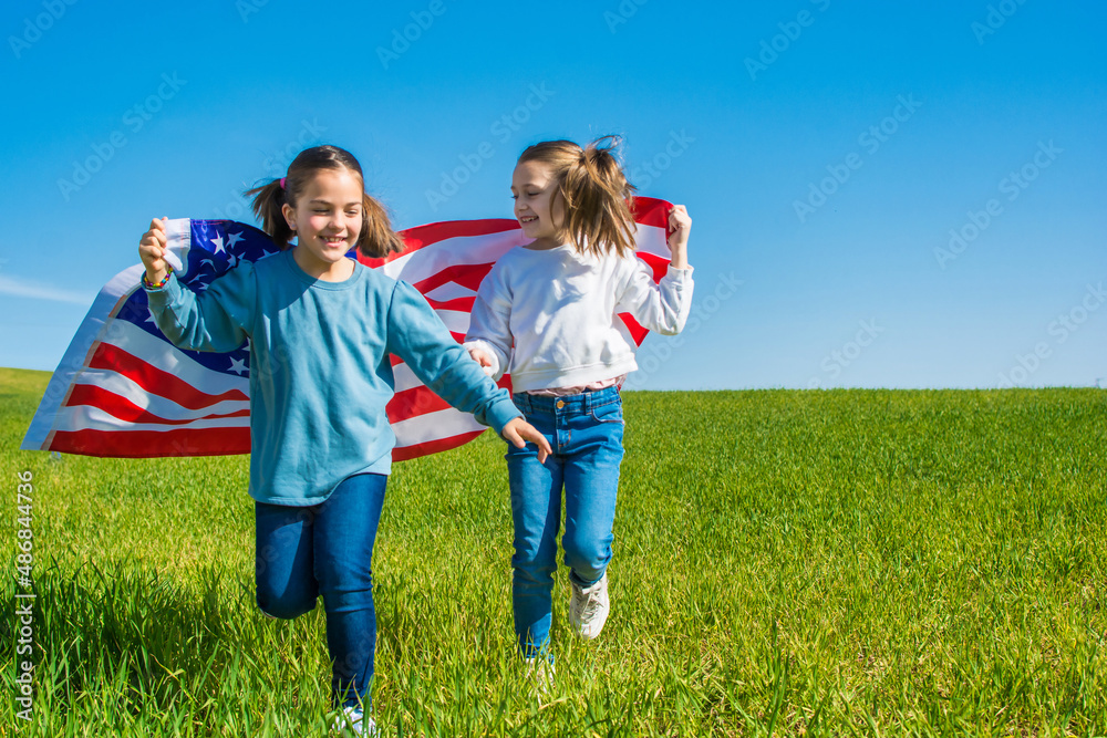 Two Beautiful Girls Running Through A Green Meadow With A Blue Sky, They Are Enjoying The 4th Of July, Showing The Flag Of The United States. Two Beautiful Girls Running Through A Green Meadow With A Blue Sky, They Are Enjoying The 4th Of July, Showing The Flag Of The United States.