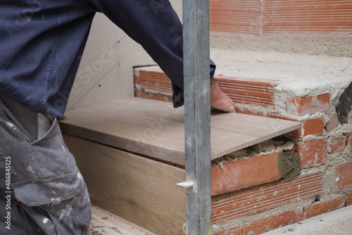 Unrecognizable bricklayer building a ceramic wood effect staircase in a home interior. House renewal. photo