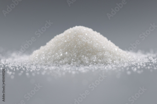 Sugar crystals pile on grey background, focus on heap of sweet powder