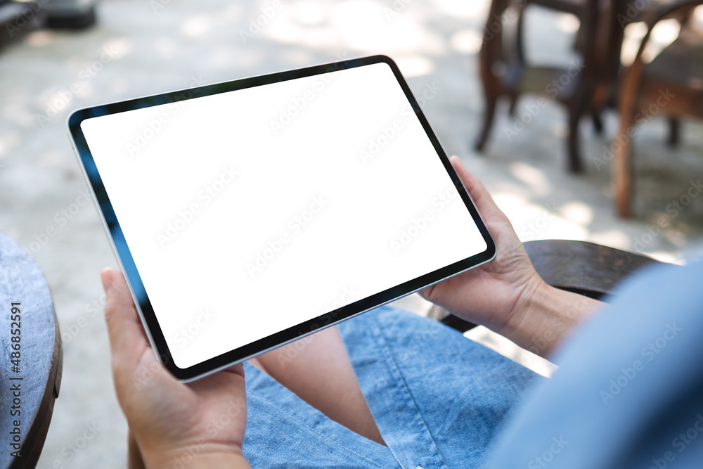 Mockup image of a woman holding digital tablet with blank white desktop screen in the outdoors