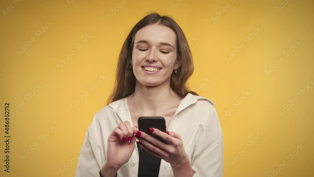 Young adult caucasian woman is online shopping on her smartphone on a bright yellow background Young adult caucasian woman is online shopping on her smartphone on a bright yellow background
