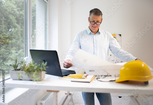 Architect with blue shirt is standing at height adjustable work table and is working photo