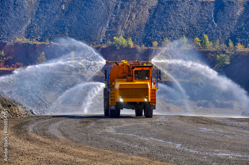 Heavy truck pours the road with water in the iron ore quarry. Dust removal, protection of the environment. Irrigation of the road from dust.