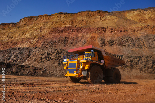 Mining dump truck transports rock, iron ore along the side of the quarry.