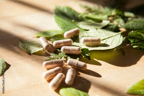 Beige vitamin medicine pills on wooden table with green leafs and window sunlight