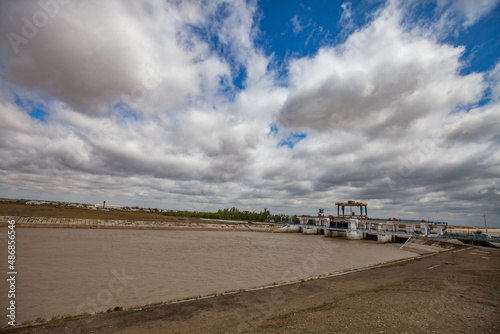 Shardara river dam near Kazaly city panorama. Gantry crane on bridge. White clouds on blue sky. Yellow water. Kyzylorda region, Kazakhstan. photo