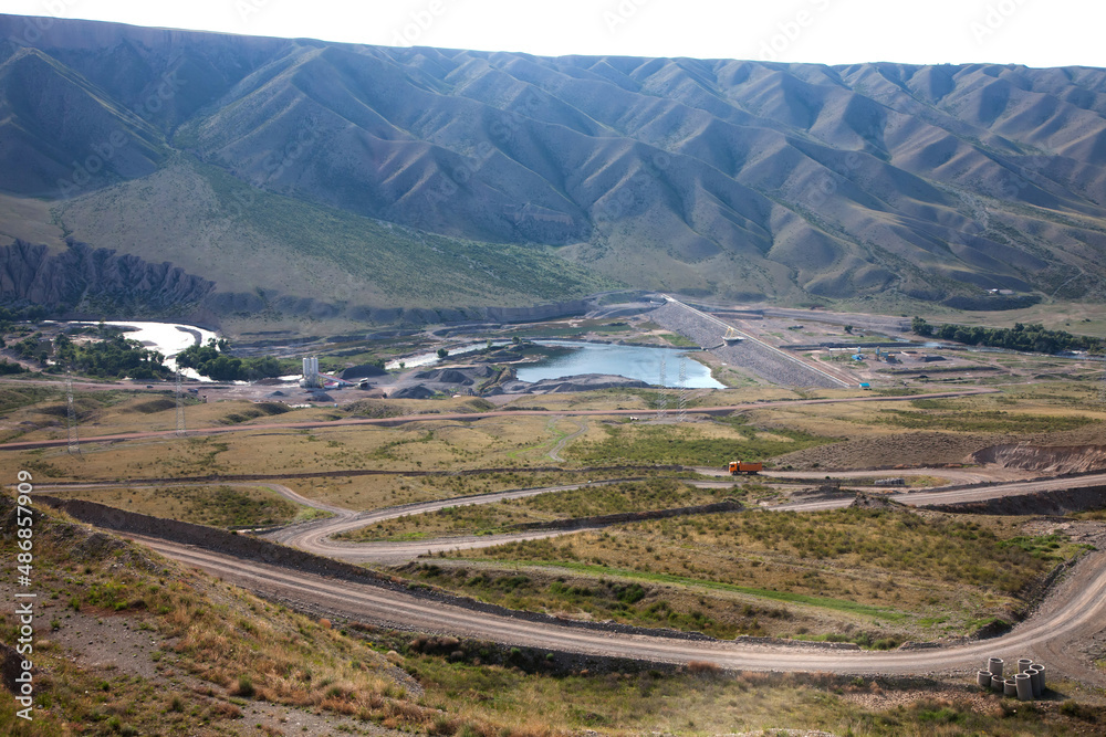 Fototapeta premium Second dam on Charyn (Sharyn) river. Asphalt roads, bridge, orange truck. Small lake. Green mountains on background.