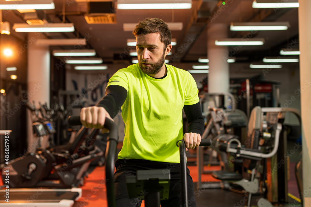 Dedicated sportsman exercising in gym. Fit male athlete is doing cardiovascular exercise. He is wearing sportswear. Dedicated sportsman exercising in gym. Fit male athlete is doing cardiovascular exercise. He is wearing sportswear.