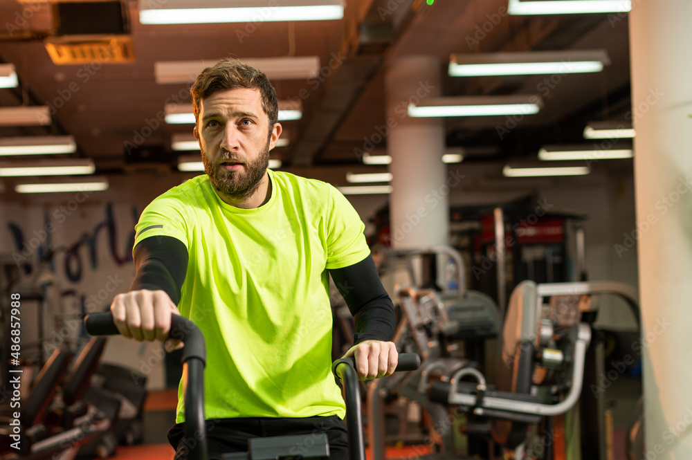 Dedicated sportsman exercising in gym. Fit male athlete is doing cardiovascular exercise. He is wearing sportswear. Dedicated sportsman exercising in gym. Fit male athlete is doing cardiovascular exercise. He is wearing sportswear.