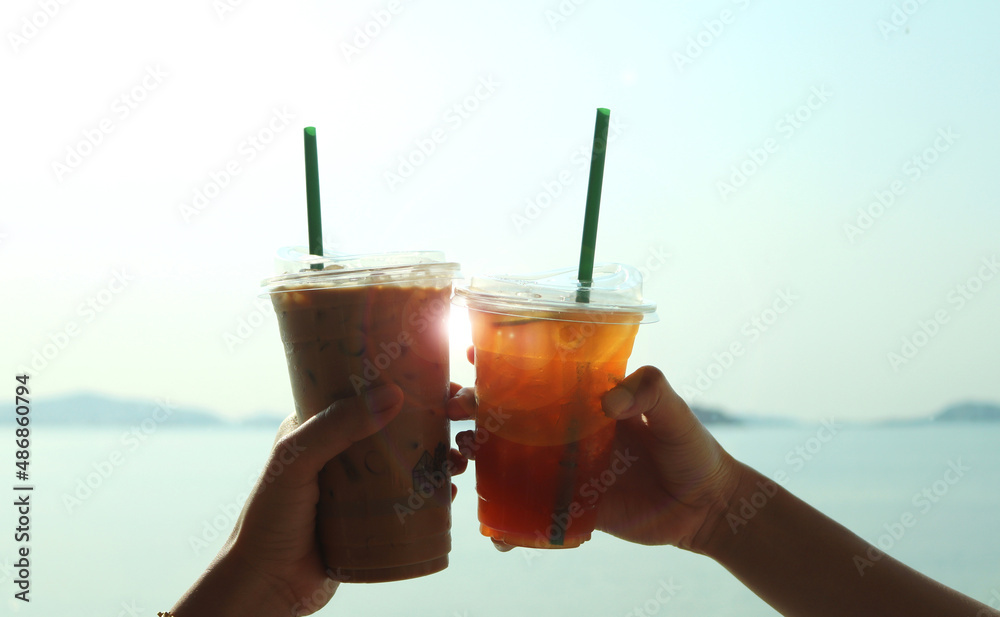 Φωτογραφία Lover couple hands holding and showing glass cup of ice lemon tea and ice espresso outdoors at the beach with blue clear water background