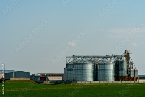 silver silos on agro manufacturing plant for processing drying cleaning and storage of agricultural products, flour, cereals and grain. Large iron barrels of grain. Granary elevator