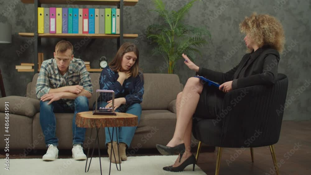Upset woman and husband with marital problems telling and sharing about relationship crisis, lack of mutual understanding and mental issues to lovely female psychologist during psychotherapy session. Upset woman and husband with marital problems telling and sharing about relationship crisis, lack of mutual understanding and mental issues to lovely female psychologist during psychotherapy session.