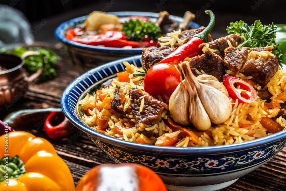 Traditional uzbek meal called pilaf. Rice with meat on plate with oriental ornament on a dark wooden background, Long banner format. space for text Traditional uzbek meal called pilaf. Rice with meat on plate with oriental ornament on a dark wooden background, Long banner format. space for text
