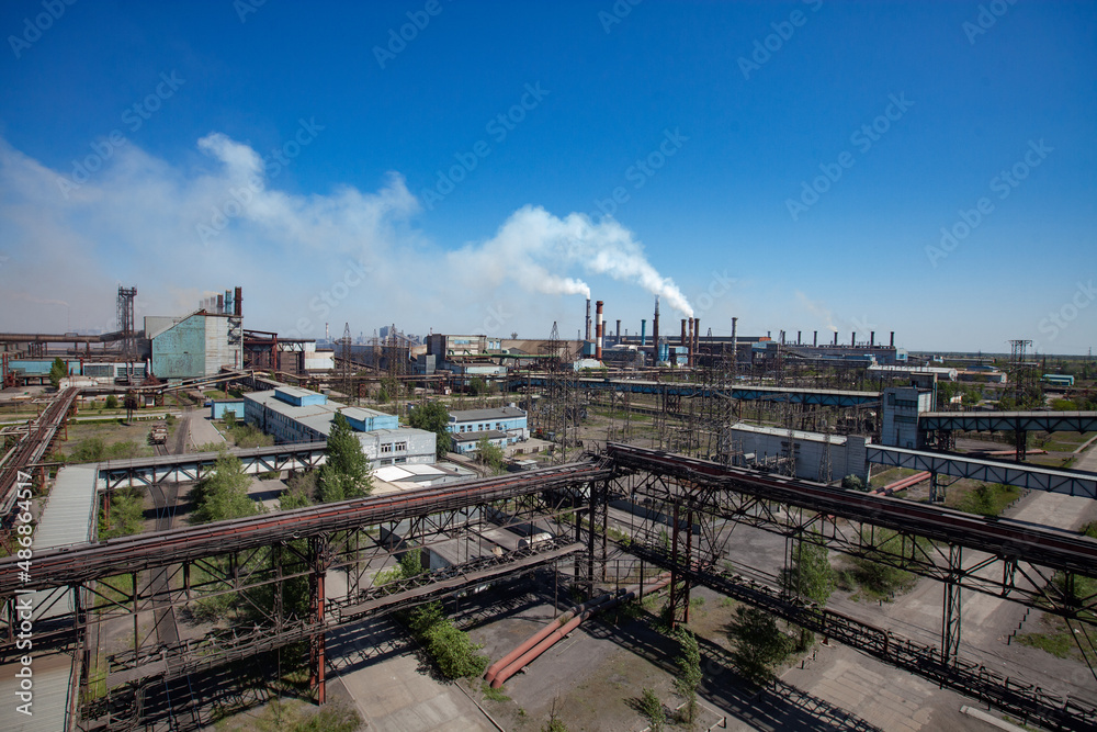 Metallurgy plant panorama view. Metal alloy production. Steel girders, pipelines and smoke stacks. Blue sky and white smoke background. Wide-angle lens.