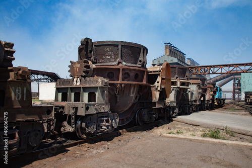 Metal alloys plant (smelter). Train on rails. Blue locomotive and rusted wagon. Metallurgical plant main industrial building on background.