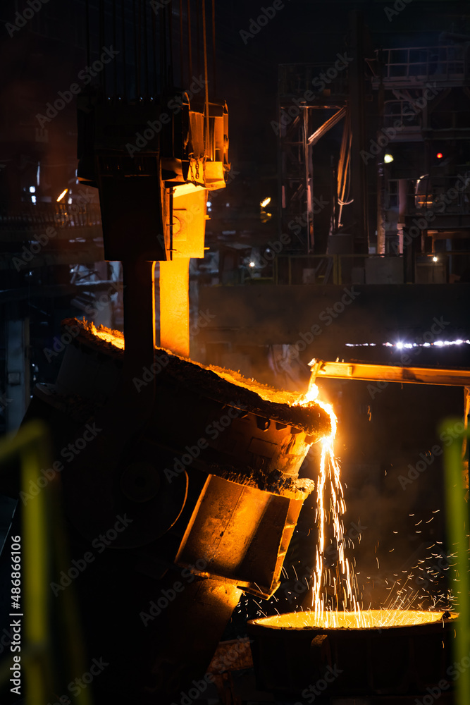Molten metal pouring from metallurgy ladle. Dark tones photo.