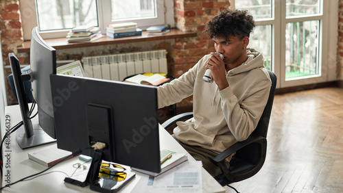 Fotografie Multiethnic male student or freelancer drink energy drink during work or study