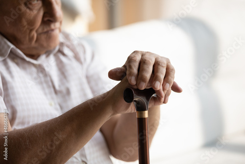 Older man hands leaning on walking cane  holding knob  handle. Mature 80s man suffering from disability  joints  bones disease  getting problems with mobility  health. Cropped shot  close up