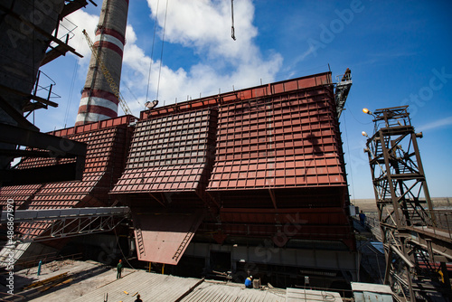 GRES-1 thermal power station. Modernization of plant. New coal bunkers and small people down. Metal tower right. Smoke stack with white smoke on background. Ekibastuz, Pavlodar region, Kazakhstan.