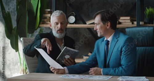 Two mature business men in a corporate office meeting. Males buisness partners discussing planning business project brainstorm while sitting at office desk