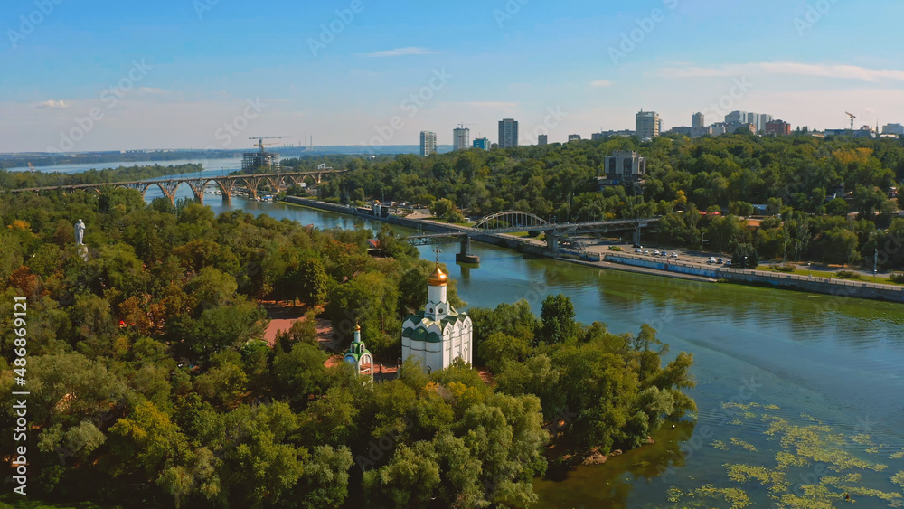 Beautiful summer landscape while sunset over the river with a church. Beautiful  urban environment - drone shooting.  Aerial view on a green island  in the town.
