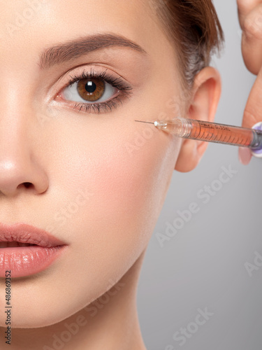 Woman getting cosmetic injection of botox in face, closeup. Injecting near eye. Woman in beauty salon, plastic surgery clinic. Cosmetology procedures concept. Beauty treatment therapy.