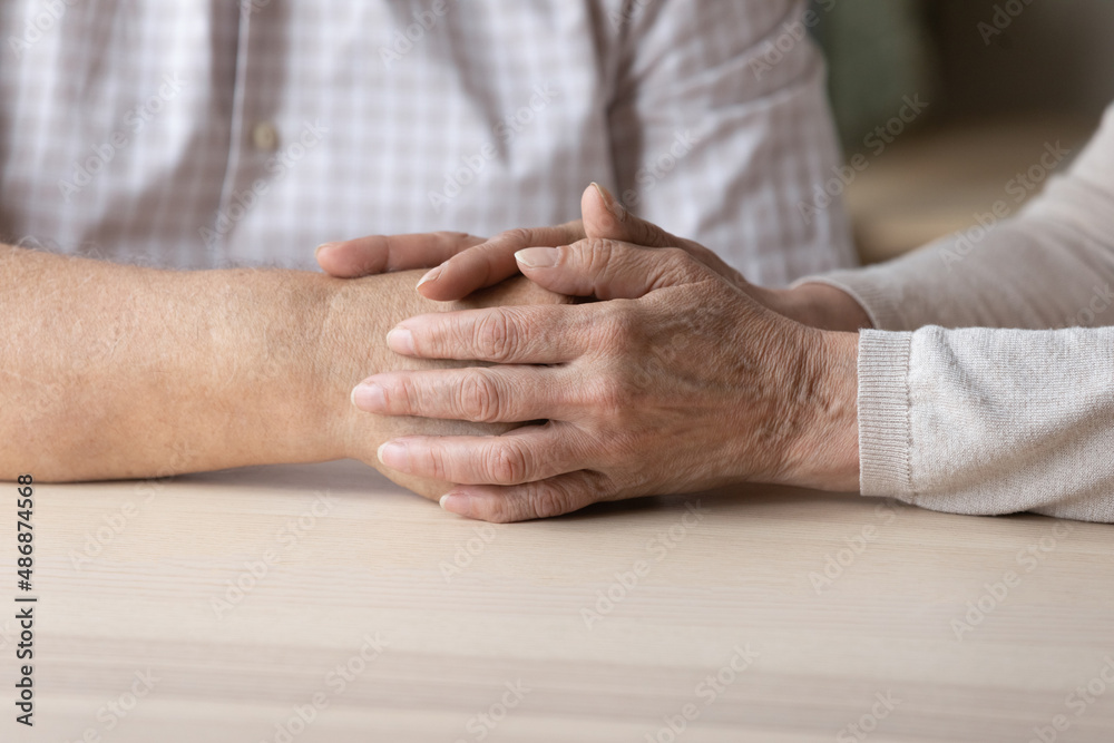 Fototapeta premium Senior loving wife holding hand of older husband, giving support, love, compassion, comfort. Mature couple going through stress, problems together. Hand touch close up. Marriage, relationships concept