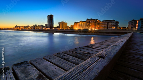 Jesolo seaside seen during the blue hour after sunset with blue sky and city lights seen from the wooden jetty on the beach. photo