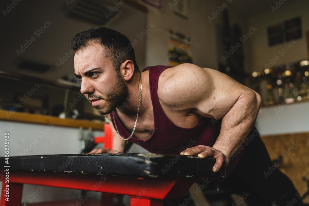 Fototapeta premium One man young adult bodybuilder doing push ups exercise training in the gym side view