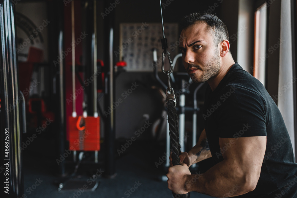 One man side view caucasian male bodybuilder at gym wearing black shirt using rope and cable weights for arms exercise muscular triceps training copy space waist up dark photo real people bodybuilding One man side view caucasian male bodybuilder at gym wearing black shirt using rope and cable weights for arms exercise muscular triceps training copy space waist up dark photo real people bodybuilding