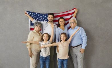 Patriotic holiday. Portrait of happy three generations family with american flag on gray background. Older grandparents with their children and two granddaughters twins smile looking at the camera.