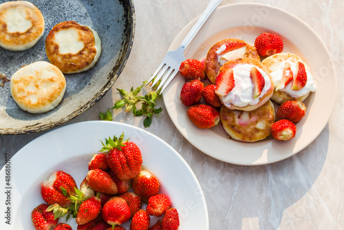 Cheesecakes with strawberries and sour cream. Breakfast in nature. Traditional Russian and Ukrainian dish.