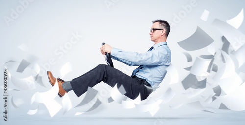 Billede på lærred Confident businessman in shirt, tie and glasses flies through sheets of white paper holding a car steering wheel, on blue background