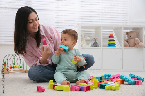 Cute baby boy playing with mother and building blocks on floor at home