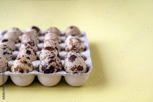 quail eggs in cardboard box on yellow background. Close-up. The idea of healthy breakfast, symbol of Easter. Copy space