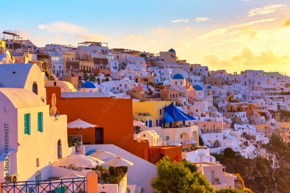 Famous Oia village with white houses and blue dome churches during sunrise on Santorini island, Aegean sea, Greece.