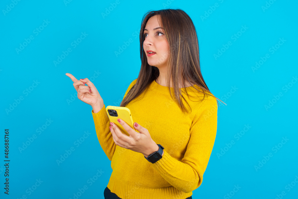 Stunned Young arab woman wearing knitted sweater over blue backgtound points sideways right copy space, recommends product, sees astonishing thing Stunned Young arab woman wearing knitted sweater over blue backgtound points sideways right copy space, recommends product, sees astonishing thing
