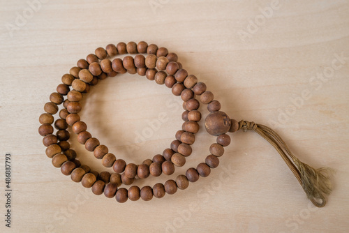 A circular brown bead necklace on the wooden table background. The necklace has the symbol of Buddhism and a bundle of the skein.