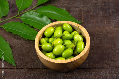 Fresh Neem fruit on wooden bowl and neem green leaf on rustic wooden background.