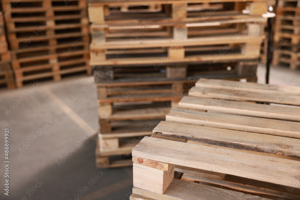 Many empty wooden pallets stacked in warehouse, closeup. Space for text Many empty wooden pallets stacked in warehouse, closeup. Space for text