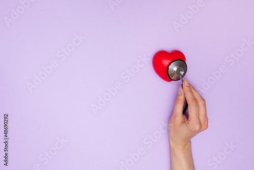 Woman doctor listens to work heart with stethoscope on purple background, flat lay.