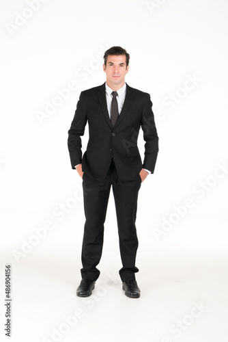 Portrait of a smiling western business man wearing a black suit with his hands in his pants pocket at studio shot on white background.