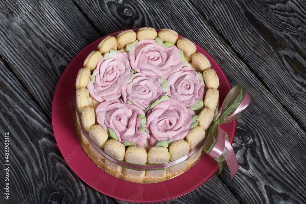 Cake with Savoiardi cookies and marshmallow roses. Tied with ribbon. The ribbon is tied into a bow.