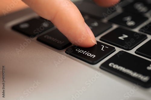 Hand pressing option key on modern laptop keyboard. Option sign and symbol close-up