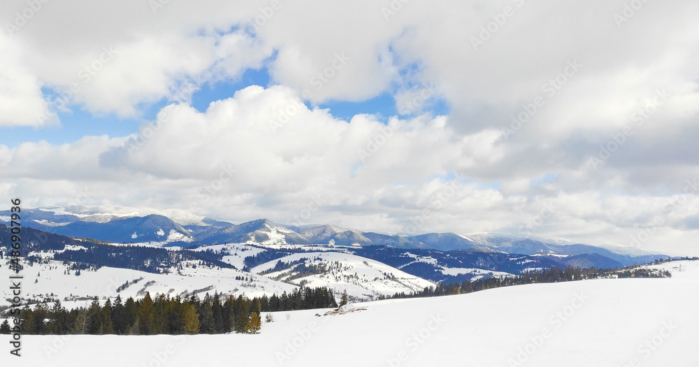 winter nature background. Panoramic landscape. Snow-capped mountains in the background, winter forest, blue sky in clouds, frost and sun.