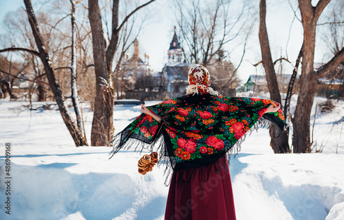 Outdoors lifestyle portrait of pretty woman in a traditional Russian headscarf with bagels on winter background. Dancing on the folk fest. Wearing Russian folk clothes. Back view. Maslenitsa festival
